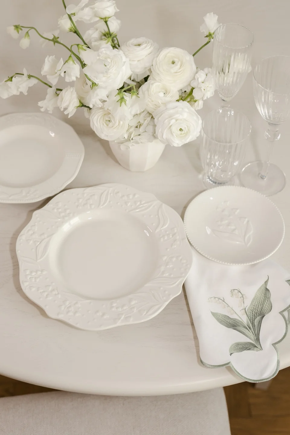 Lily of the Valley dinnerware with clear glasses, white flowers and a botanical napkin on a styled table